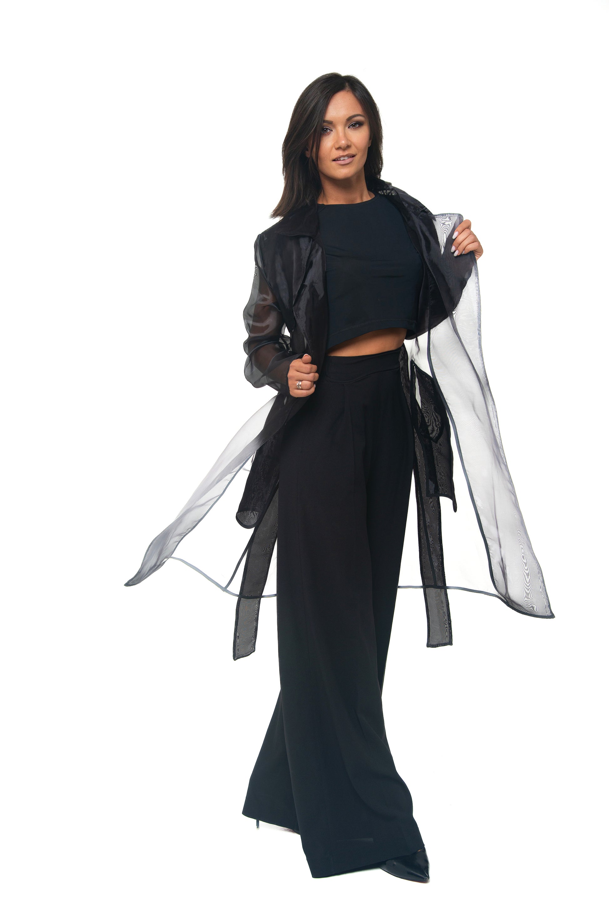 Woman wearing a black outfit with a long, sheer black trench on a white background